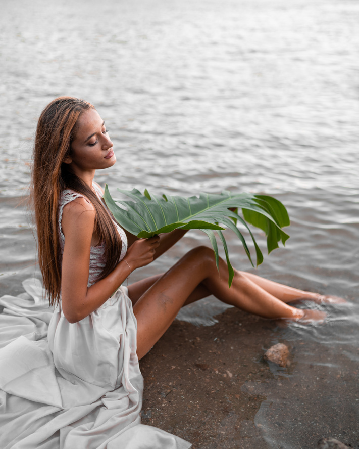 Feminine woman sitting on shallow sea with green plant leaf